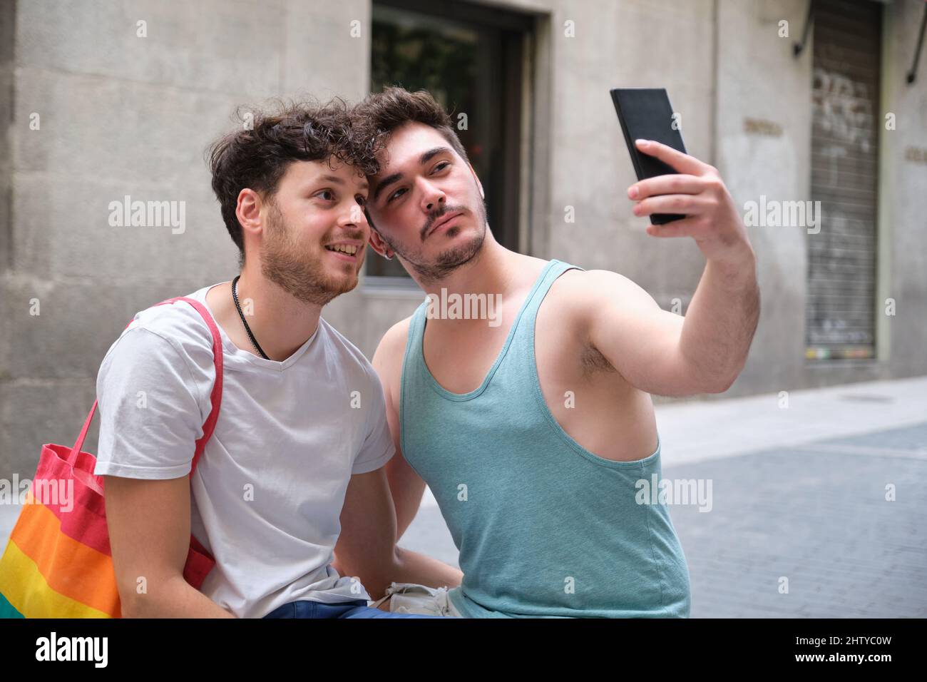 Couple gay prenant un selfie avec le smartphone assis dans la rue. Banque D'Images