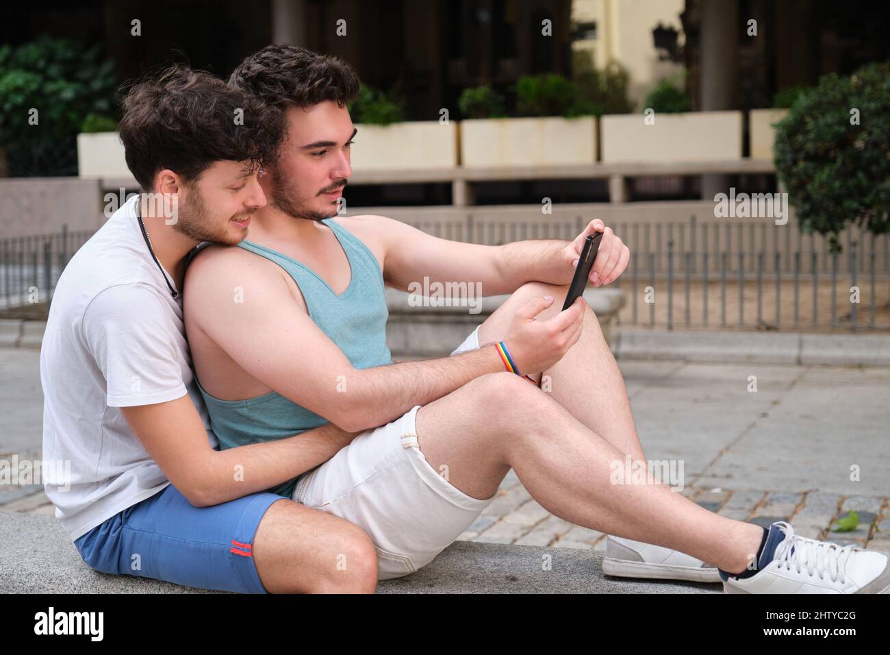 Couple gay utilisant le smartphone assis sur un banc. Banque D'Images