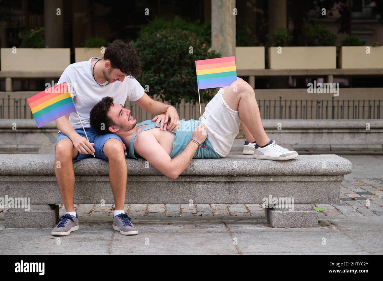 Un couple gay riant et embrassant assis sur un banc tenant des drapeaux LGBT. Banque D'Images