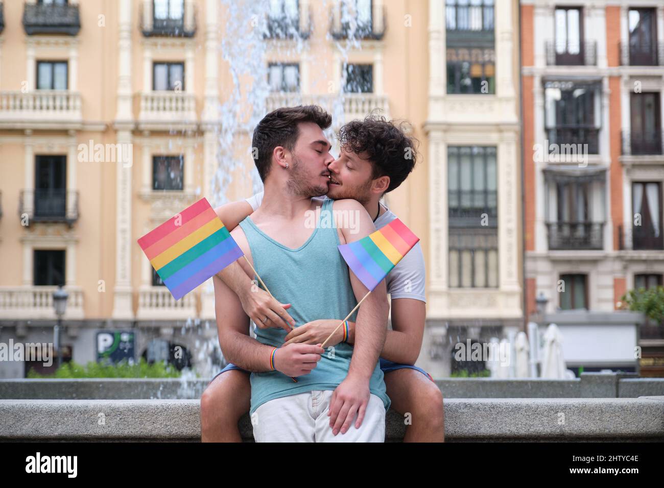 Un couple gay riant et embrassant assis sur un banc tenant des drapeaux LGBT. Banque D'Images