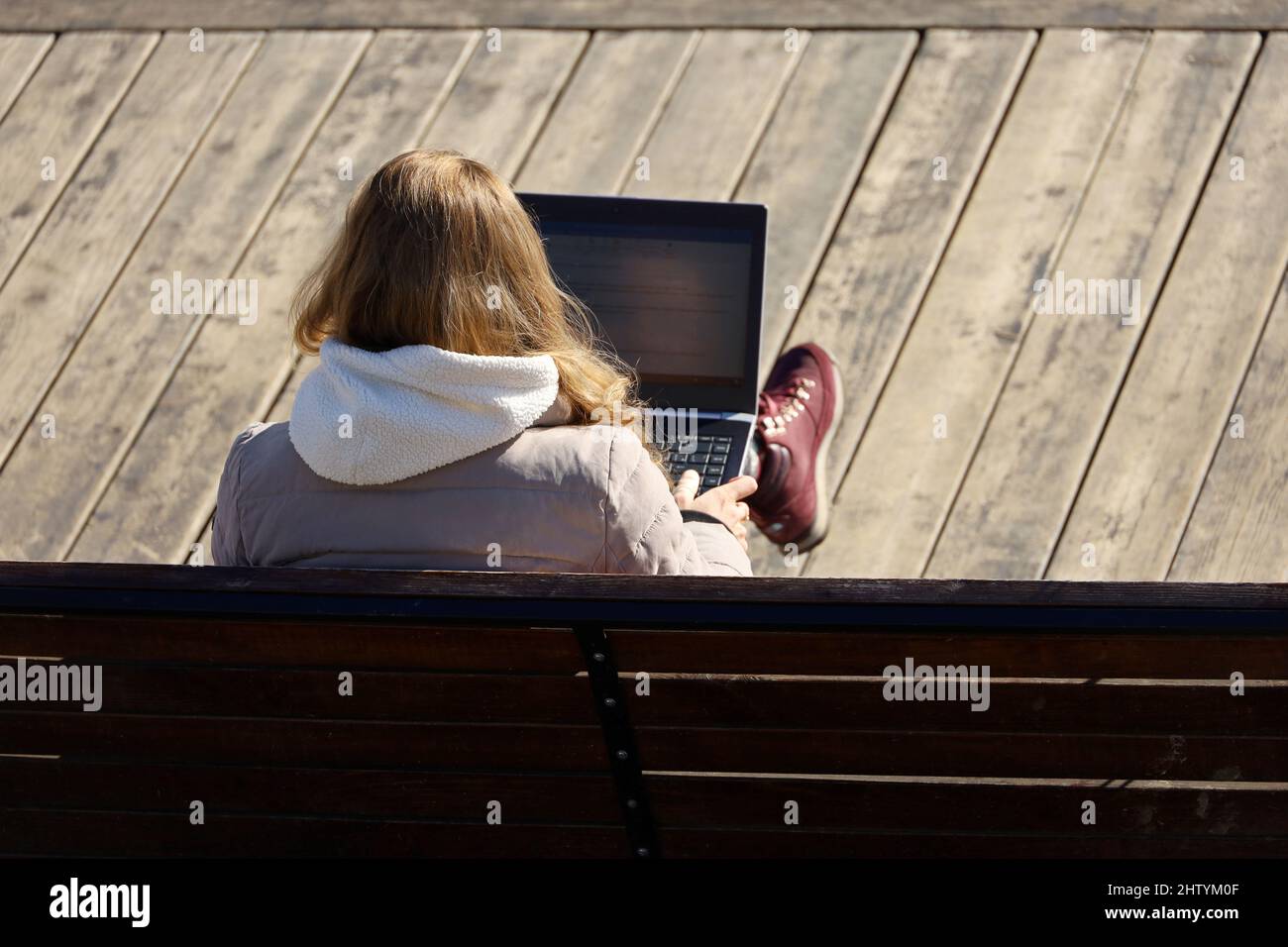 Fille assise avec un ordinateur portable sur ses genoux sur un banc en bois dans le parc de printemps. Concept de travail à distance en extérieur, indépendant Banque D'Images