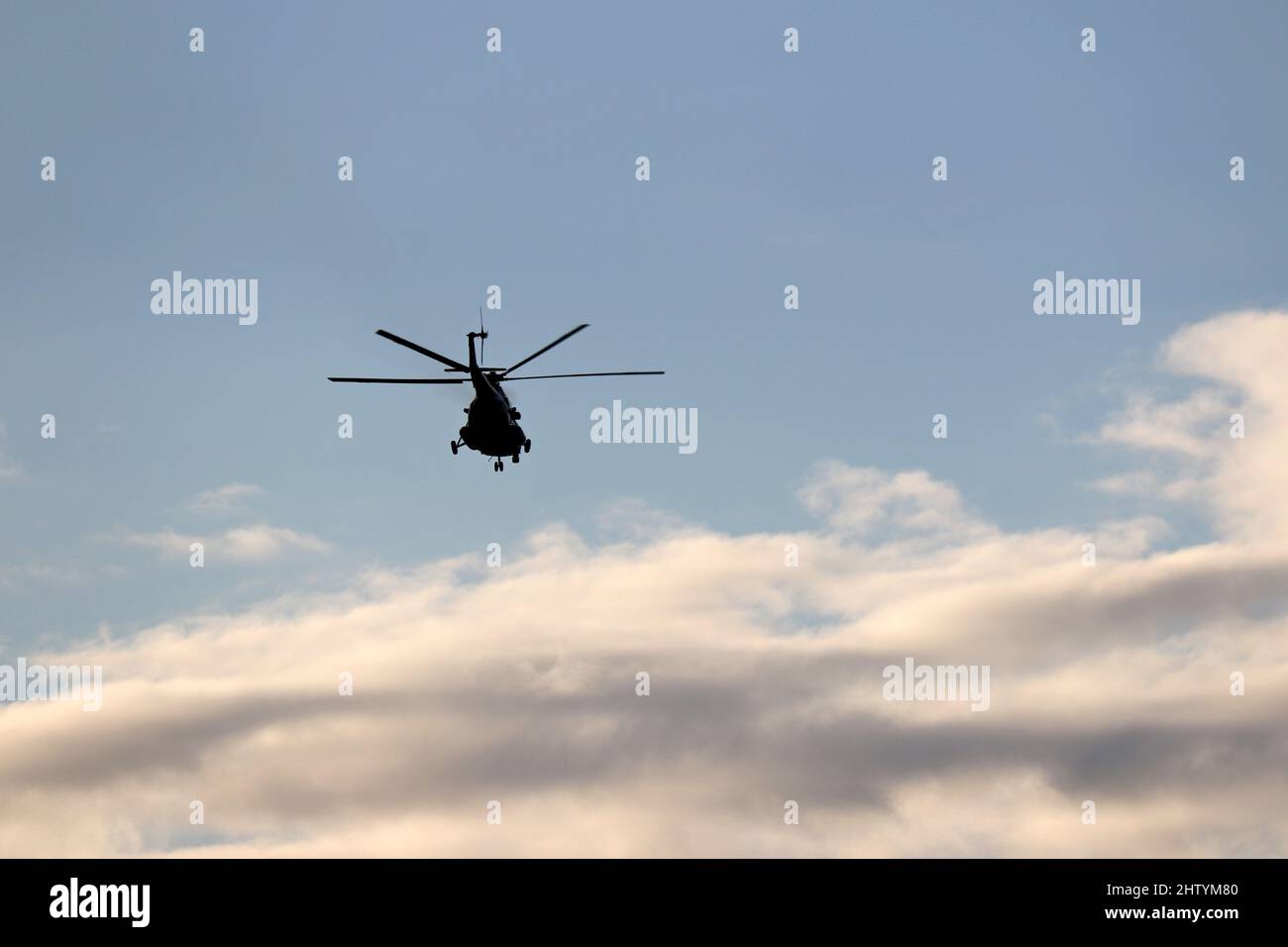Silhouette d'hélicoptère militaire en vol dans un ciel bleu avec des nuages Banque D'Images