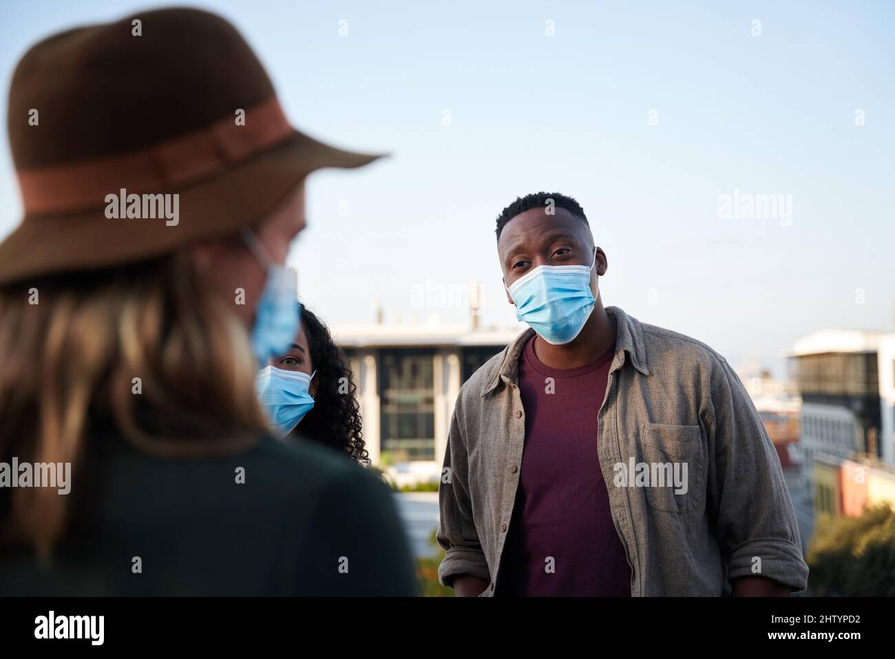 Des hommes noirs et des amis multiculturels bavardent sur un toit-terrasse avec des masques. Vie en ville et bons moments. Banque D'Images