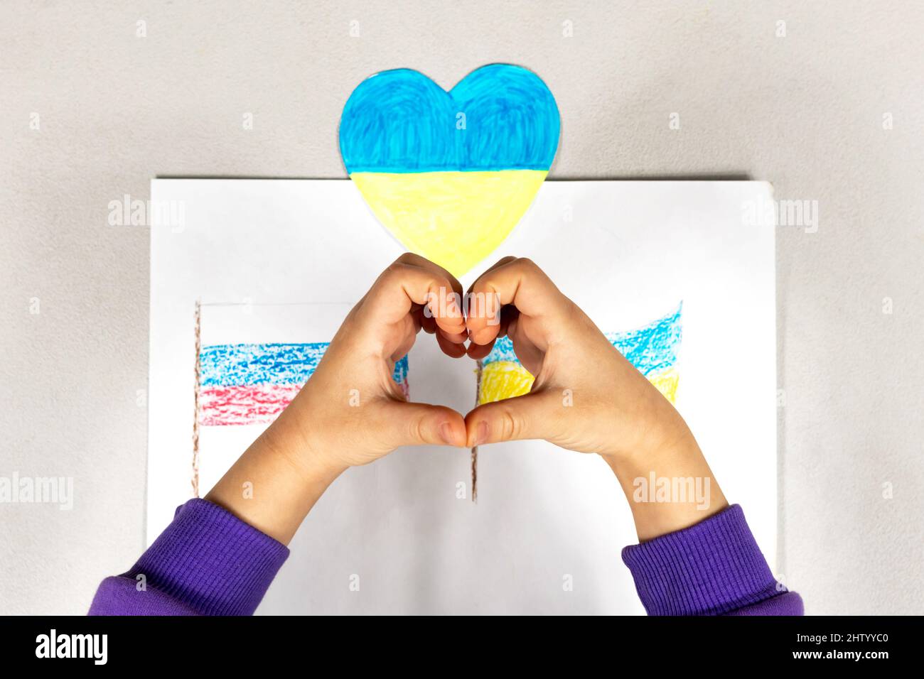 Un enfant fait un signe de coeur avec ses mains sur un dessin de deux drapeaux de l'Ukraine et de la Russie gros plan. Vue de dessus. Les enfants contre la guerre. Banque D'Images