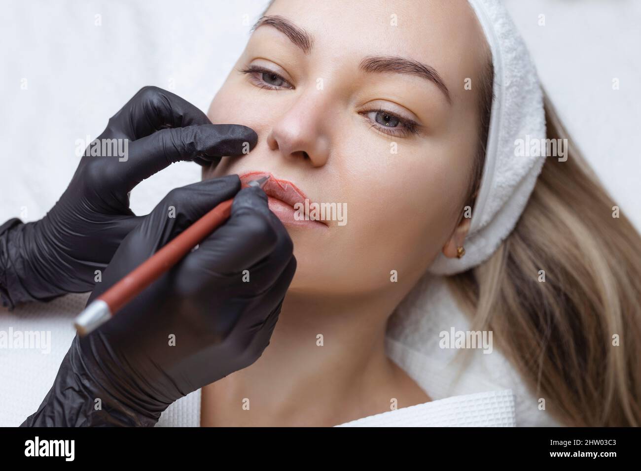 Jeune femme avec maquillage permanent sur ses lèvres dans un salon de  cosmétologues. Tatouage de maquillage permanent. Dessinez une ligne avec un  crayon rouge à lèvres Photo Stock - Alamy