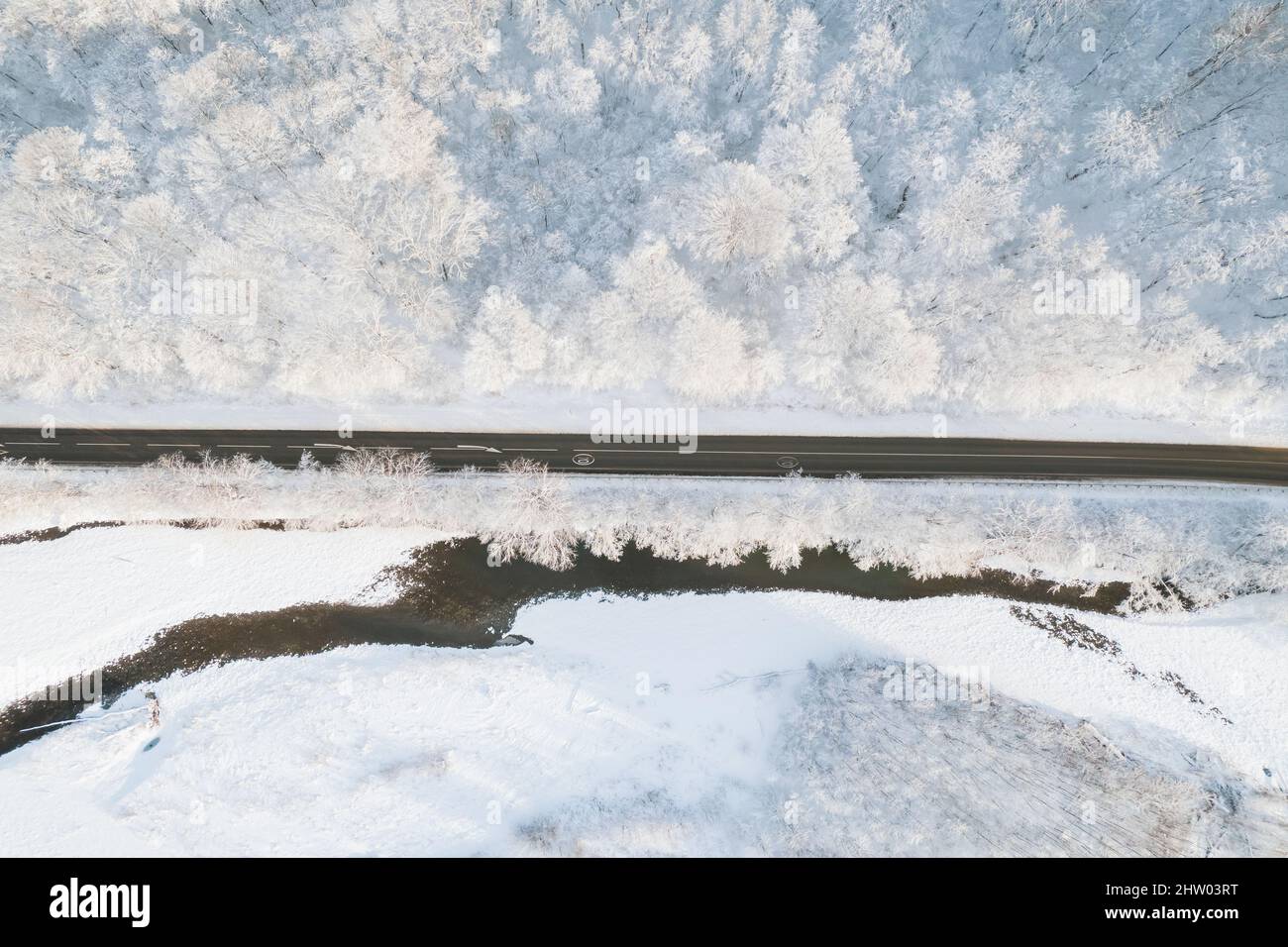 Aérienne de haut en bas cinéma hiver neige lâche route de campagne, l'asphalte serpentine. Les voitures passent la circulation dans la forêt. Banque D'Images