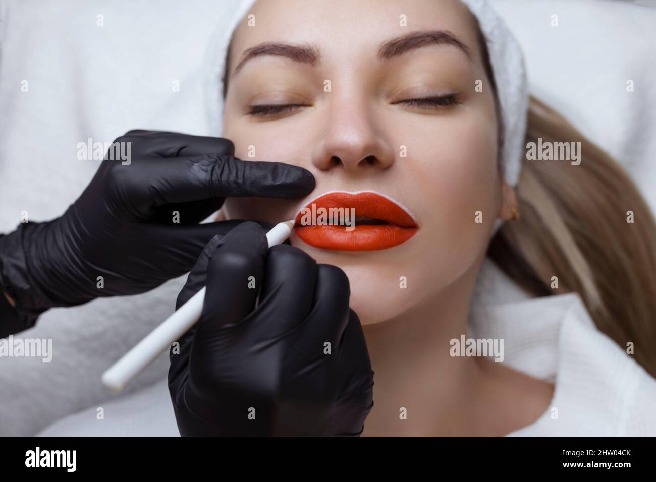 Jeune femme avec maquillage permanent sur ses lèvres dans un salon de cosmétologues. Tatouage de maquillage permanent. Dessinez une ligne avec un crayon blanc à lèvres Banque D'Images