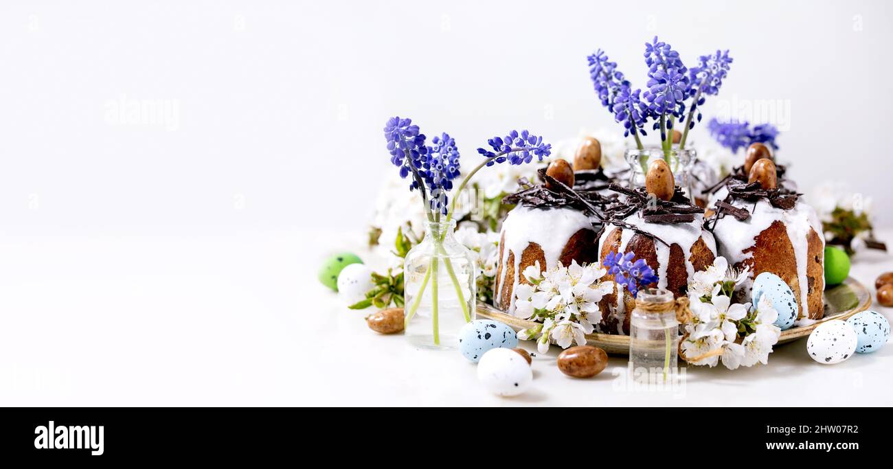 Gâteau traditionnel de Pâques maison au kulich avec nids de chocolat et œufs, branches de cerisier fleuries et fleurs de muscari. Arrière-plan blanc. Traditionnel o Banque D'Images