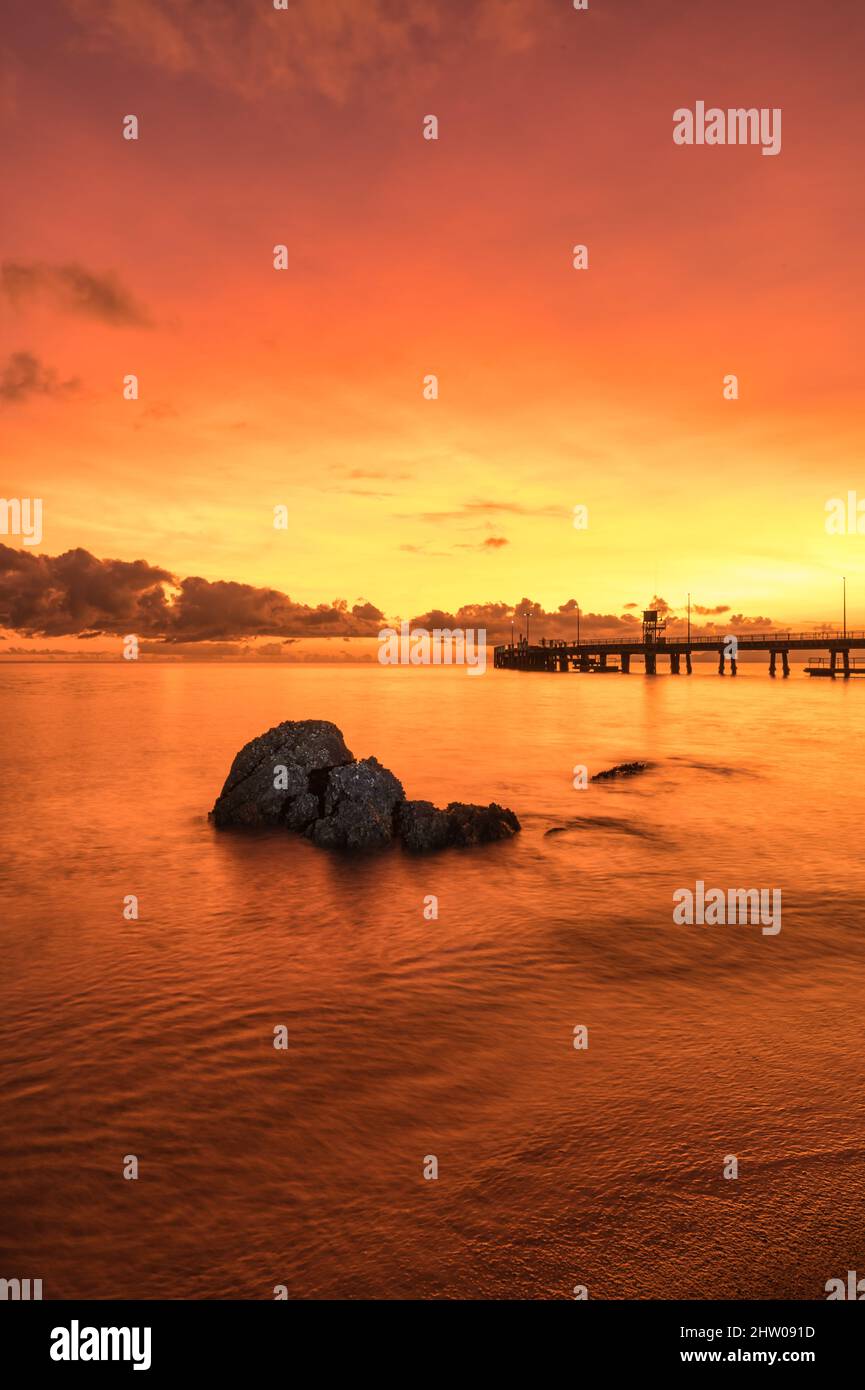 Un lever de soleil spectaculaire, vibrant, rouge/orange au-dessus de Palm Cove, avec des rochers en avant-plan incrustés d'huîtres, qui suscitent l'intérêt de l'emblématique jetée de QLD, en Australie. Banque D'Images
