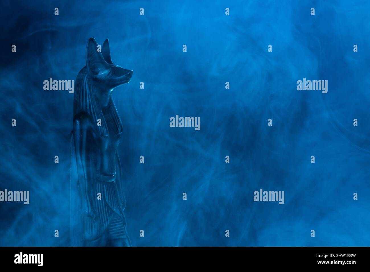 Statue égyptienne du dieu de la mort Anubis en pierre noire dans un brouillard bleu sur fond noir. Photo de haute qualité Banque D'Images