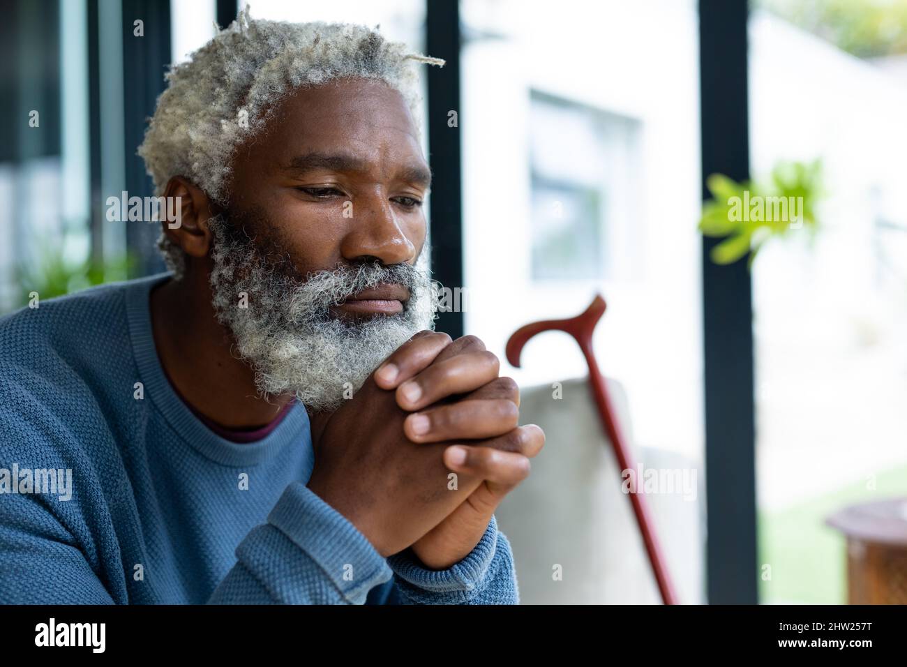 Homme afro-américain barbu avec les mains jointes sur le menton contemplant chez lui Banque D'Images