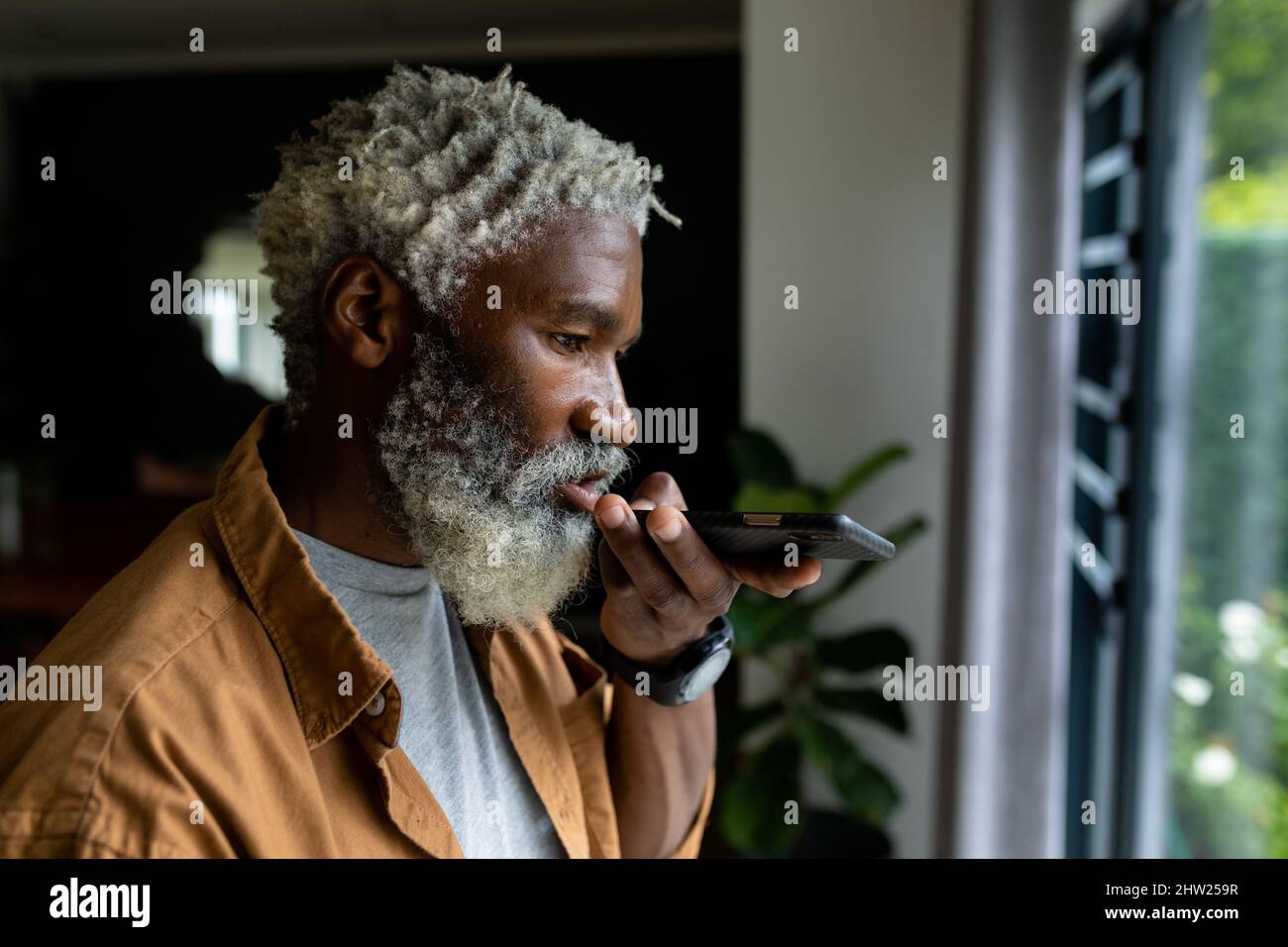 Homme afro-américain senior barbu envoyant un message vocal via smartphone Banque D'Images