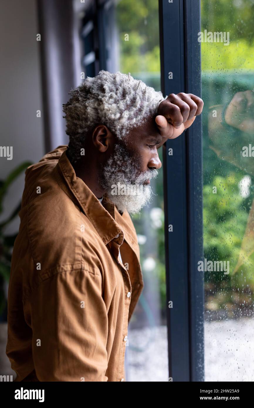 Homme senior afro-américain pendu sur une fenêtre en verre chez lui Banque D'Images