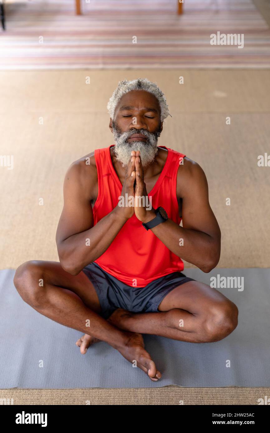Homme senior afro-américain avec les yeux fermés et les mains clastées pratiquant le yoga à la maison Banque D'Images
