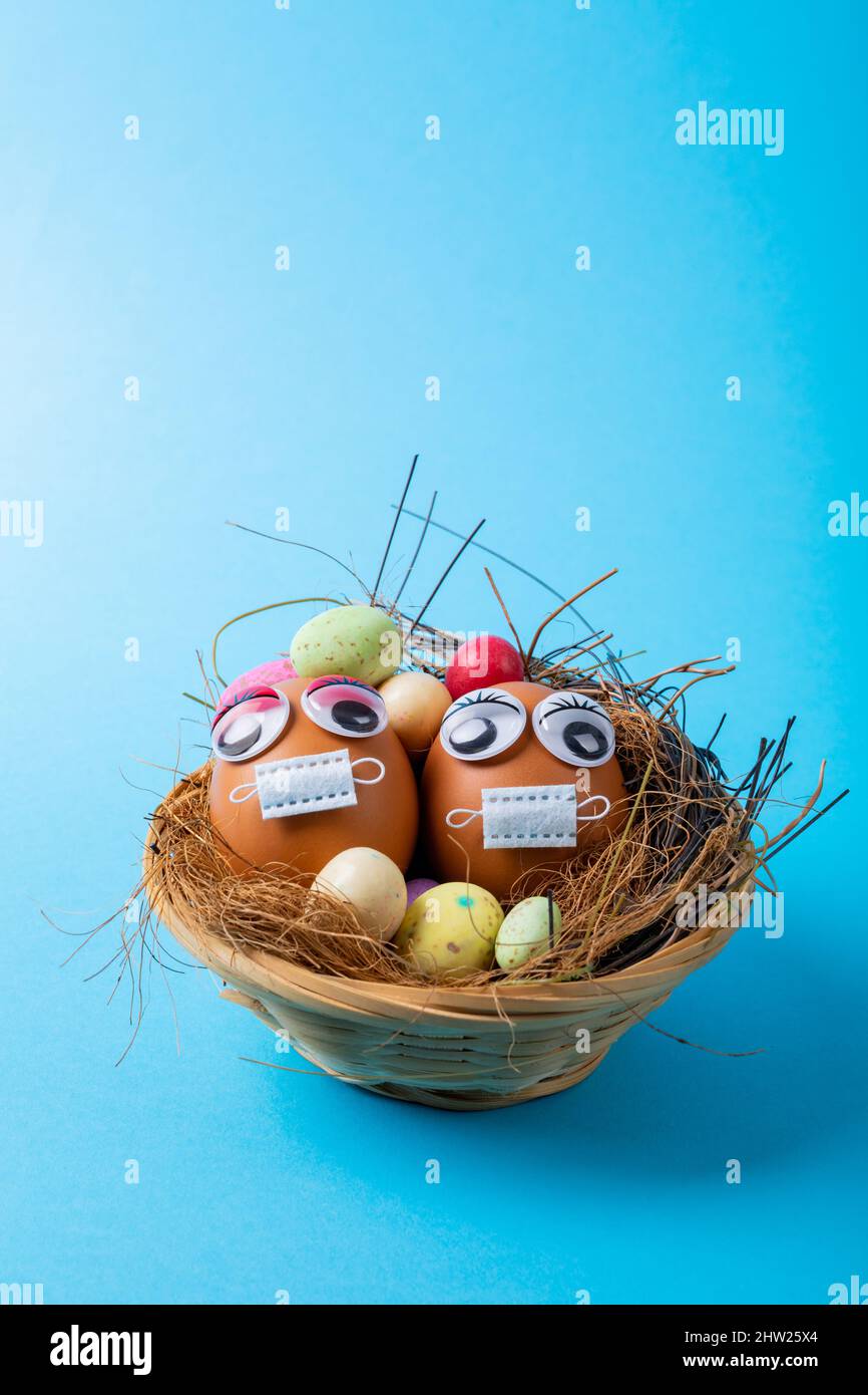 Oeufs de Pâques avec des yeux et un masque avec des bonbons et des pailles en nid sur fond bleu Banque D'Images