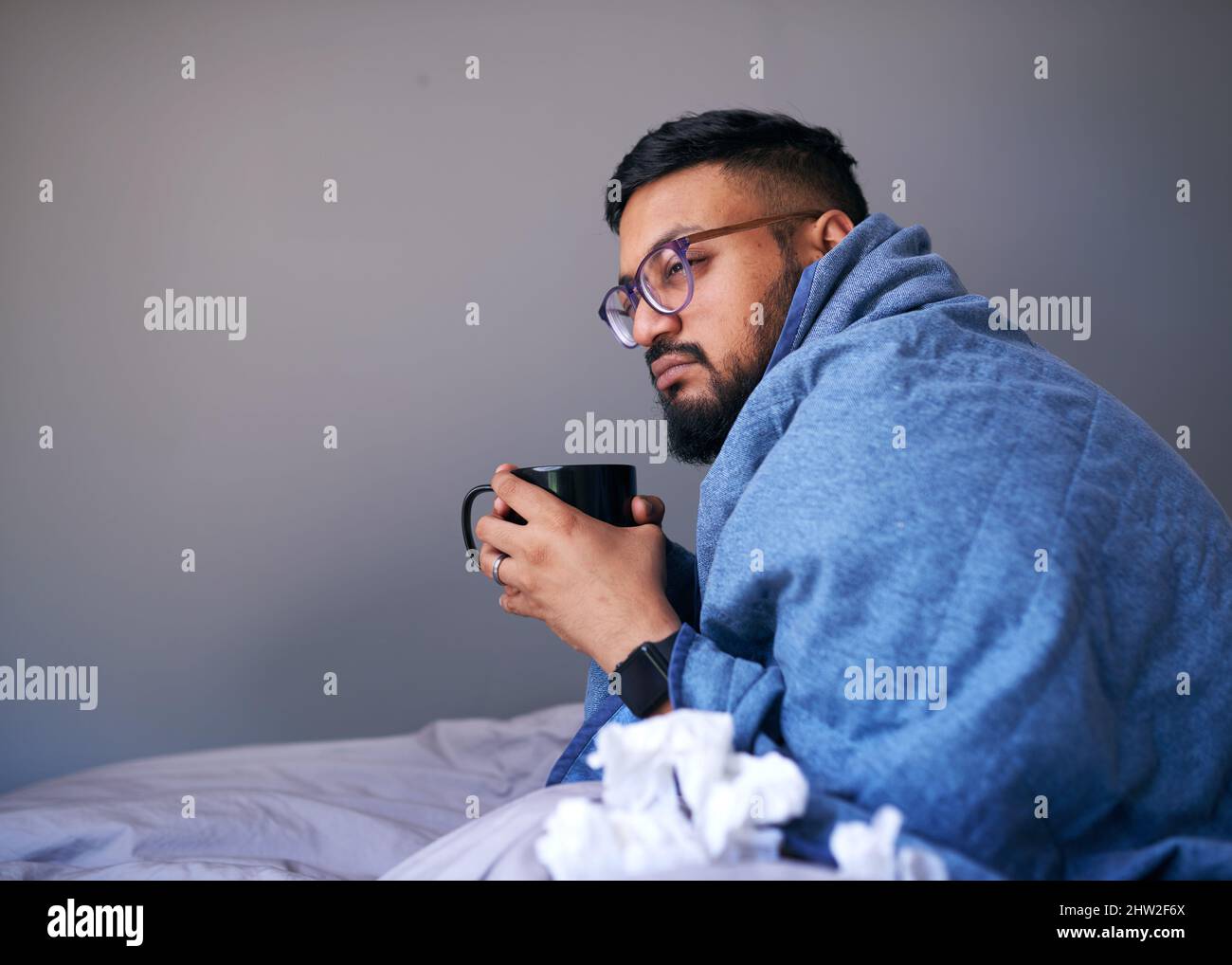 Un malade s'assoit dans un lit enveloppé dans une couverture contenant une boisson chaude. Copier l'espace Banque D'Images