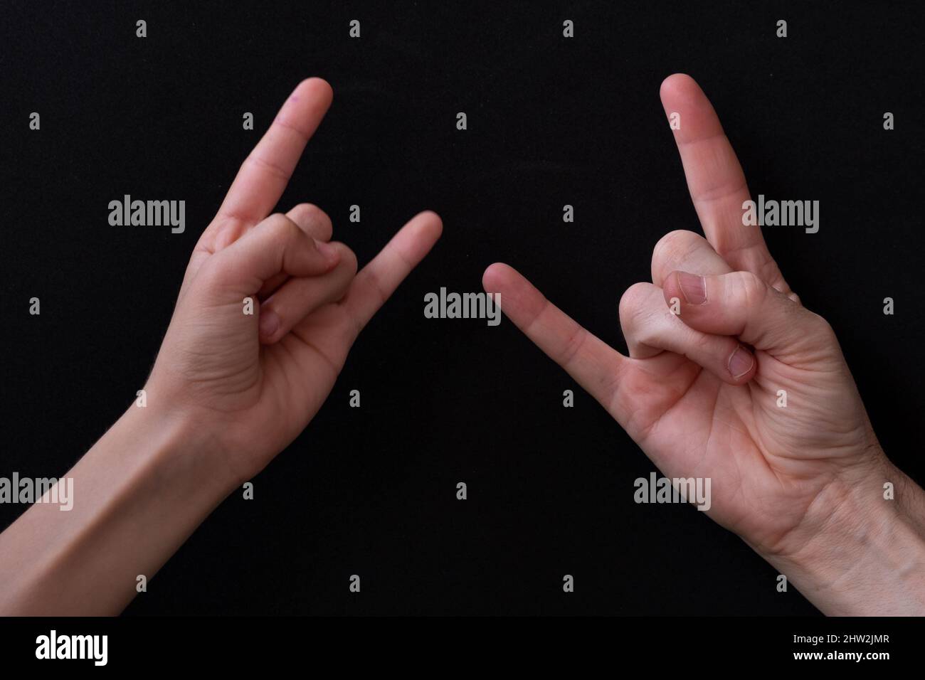 Main d'un homme et d'une femme faisant le signe des cornes sur un fond noir. Banque D'Images