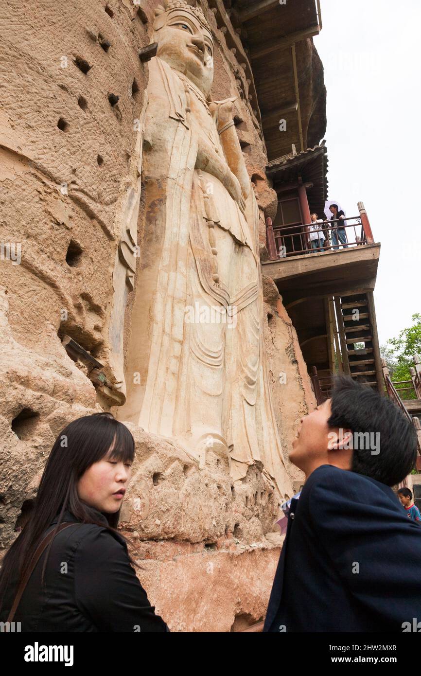 Le couple de touristes chinois voir la représentation de Bouddha figures, représentations et images bouddhistes (qui semble être restauré très récemment à l'aide de nouveaux matériaux) sur la face rockface des Grottes Maijishan, autrefois romanisé comme Maichishan, sont une série de 194 grottes coupées sur le côté de la colline de Majishan à Tianshui, Province de Gansu, Chine. (67/125) Banque D'Images