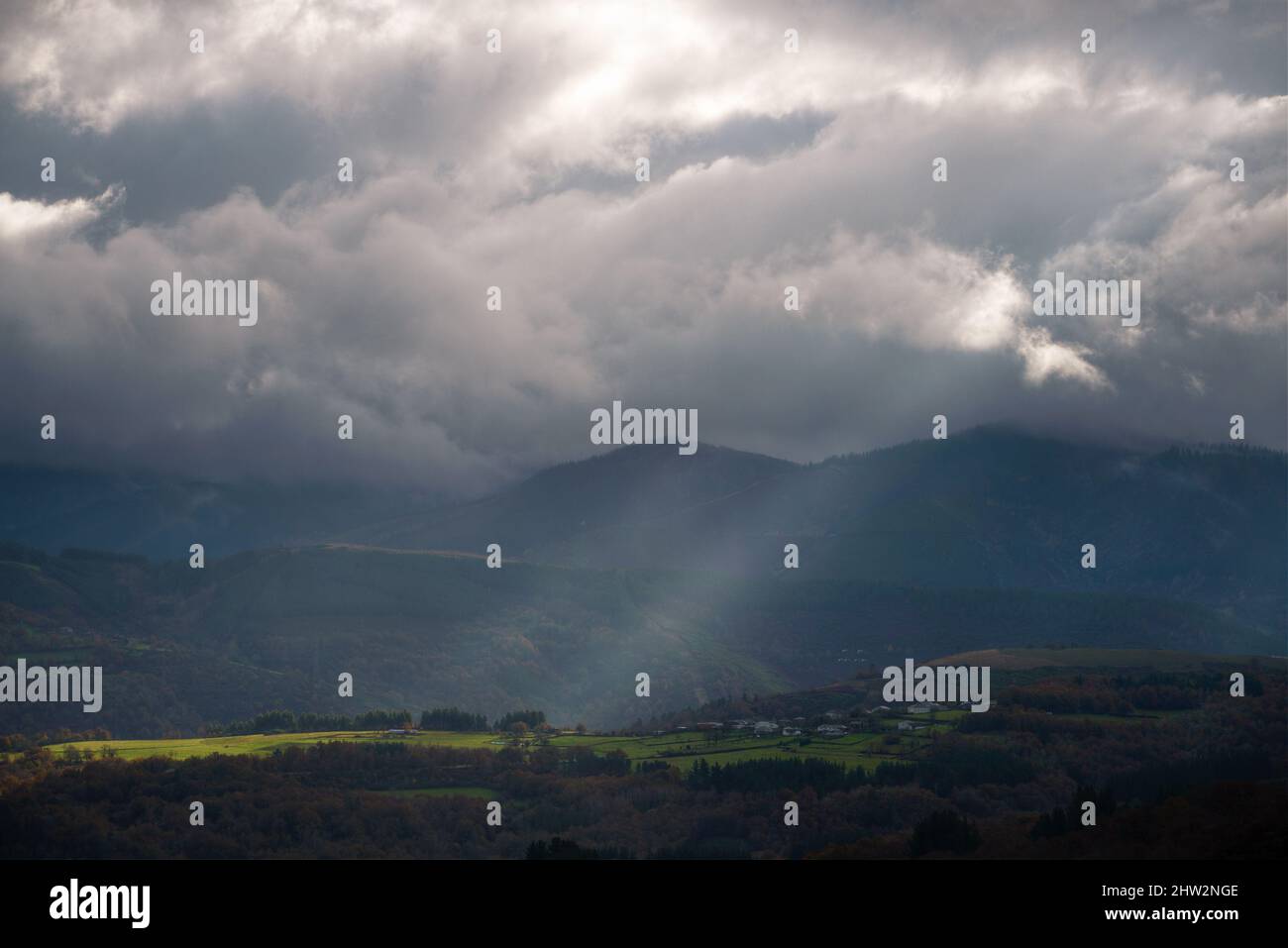 Un rayon de soleil se brise à travers les nuages et illumine quelques prairies entre les montagnes de Cervantes Ancares en Galice Banque D'Images