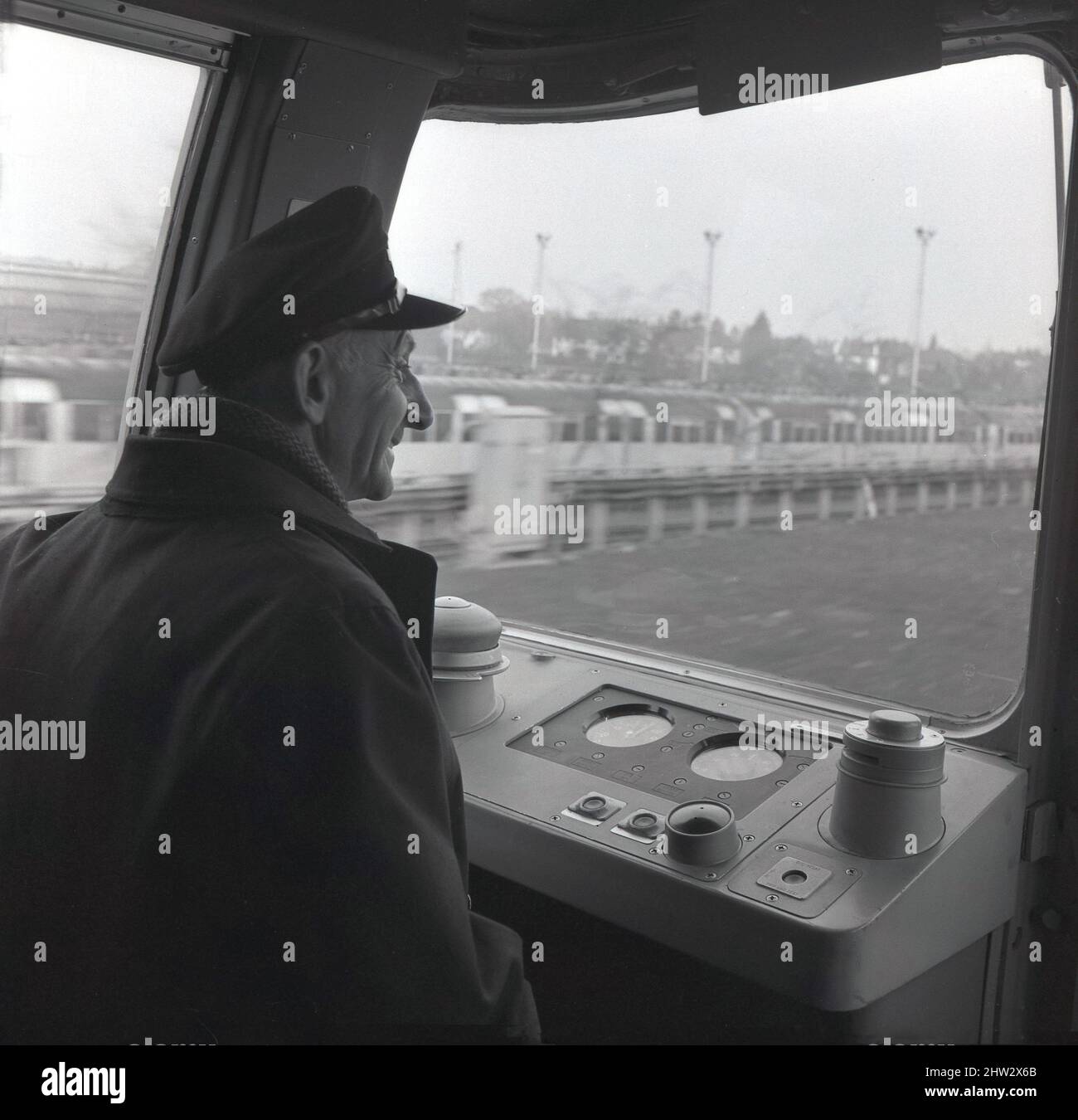 1960s, historique, un chauffeur de métro en casquette et veste, assis dans la cabine du conducteur d'un train de métro de Londres, Londres, Angleterre, Royaume-Uni. Connus sous le nom de stock de 1967, les trains opéraient pour la première fois sur la ligne Victoria nouvellement ouverte en 1968 et étaient en service jusqu'en 2011. Équipés du système d'exploitation automatique des trains (ATO), ils ont été les premiers trains automatiques au monde. Ils ont également été le premier matériel roulant souterrain de Londres à présenter des fenêtres enveloppantes dans la cabine du conducteur. Banque D'Images