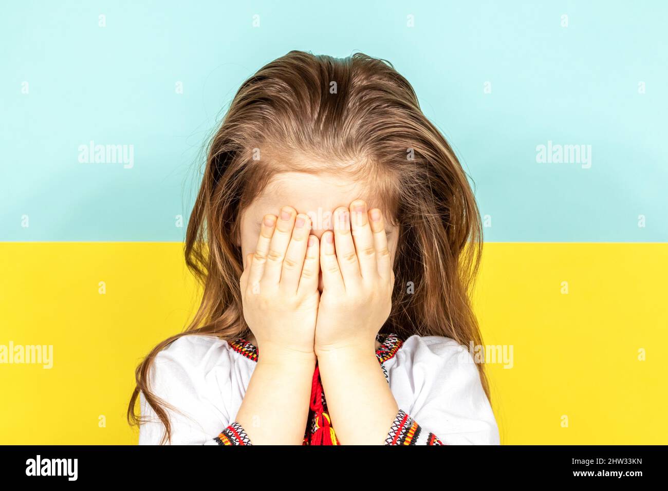 Une jeune fille dans une chemise ukrainienne nationale à motif brodé est en train de pleurer, couvrant son visage avec ses mains sur le fond du drapeau ukrainien Banque D'Images