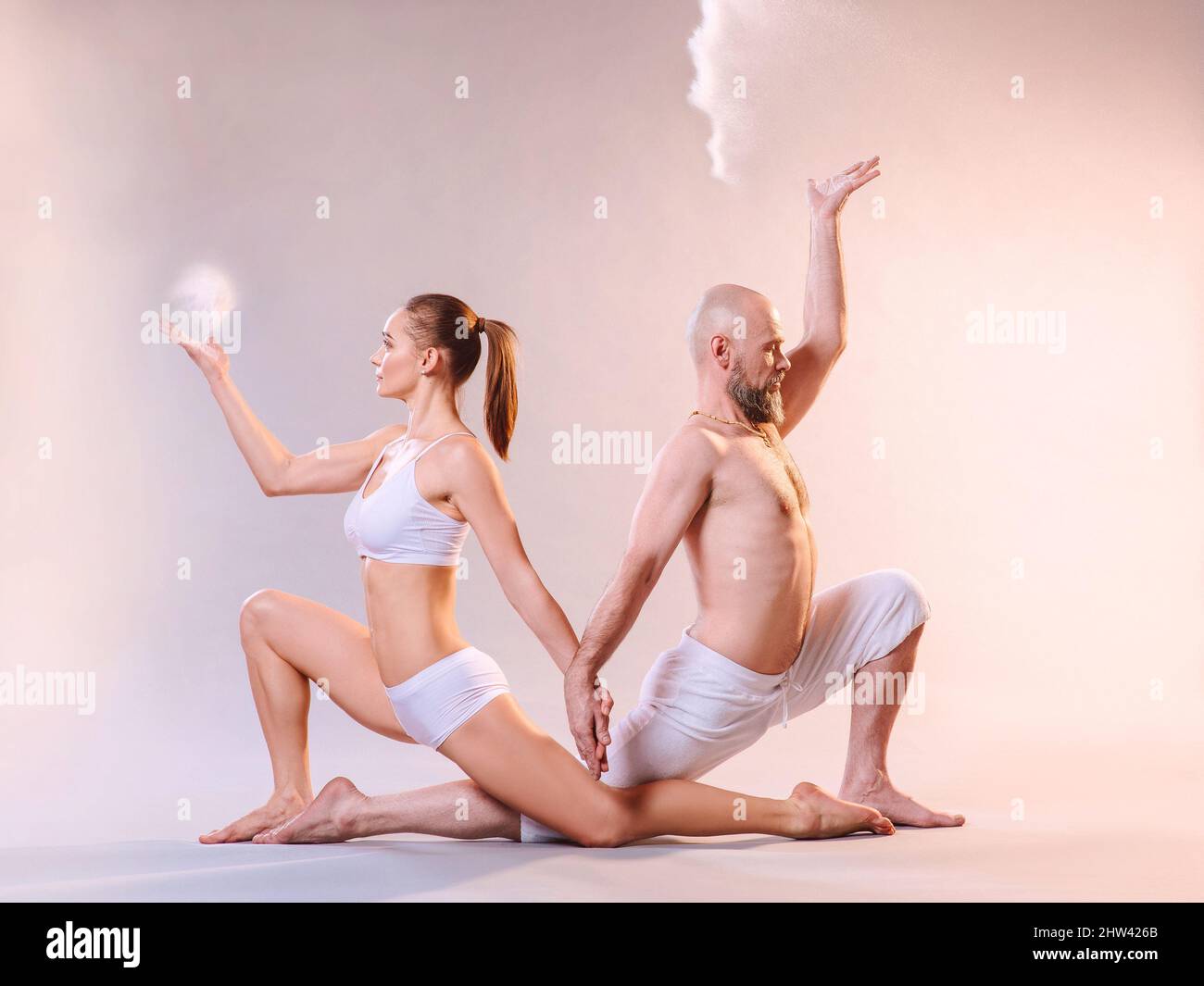 Belle femme sportive et homme dans des vêtements blancs faisant des asanas de yoga avec le sable coloré intérieur Banque D'Images