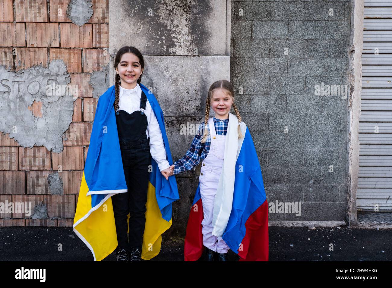 Petites filles avec des drapeaux ukrainiens et russes devant un mur détruit par des bombes. Ukraine russie conflit 2022 escalade. Concept de paix Banque D'Images