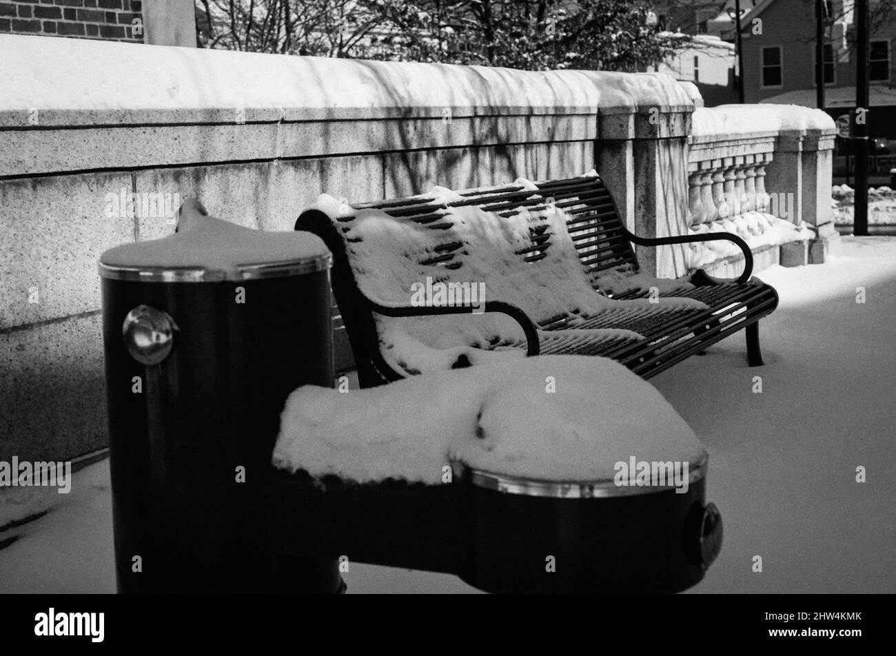 Une fontaine et un banc de parc couverts de neige se trouvent contre le mur de pierre après la tempête. Banque D'Images