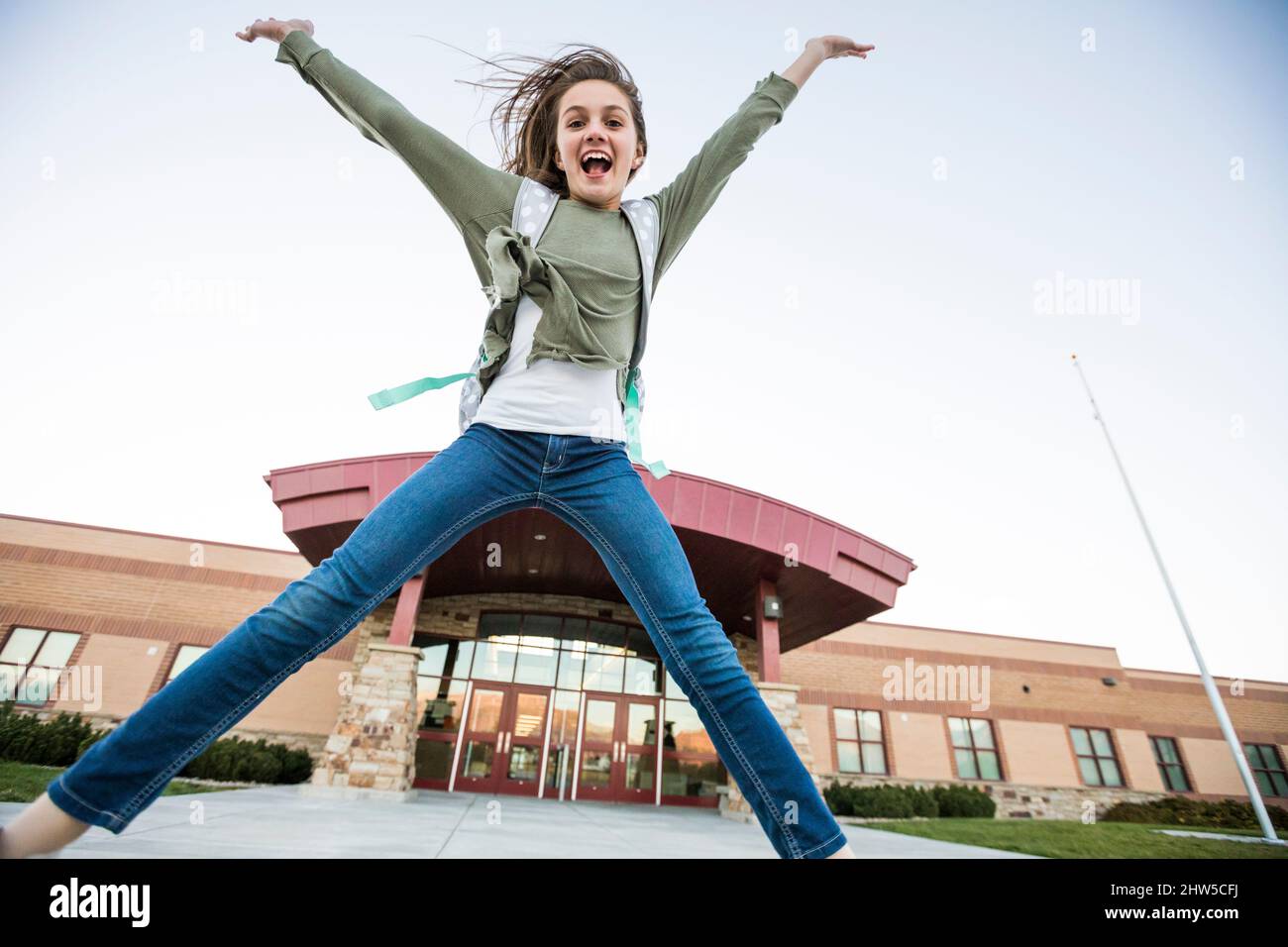 États-Unis, Utah, Lehi, fille souriante (12-13) sautant devant le bâtiment de l'école Banque D'Images