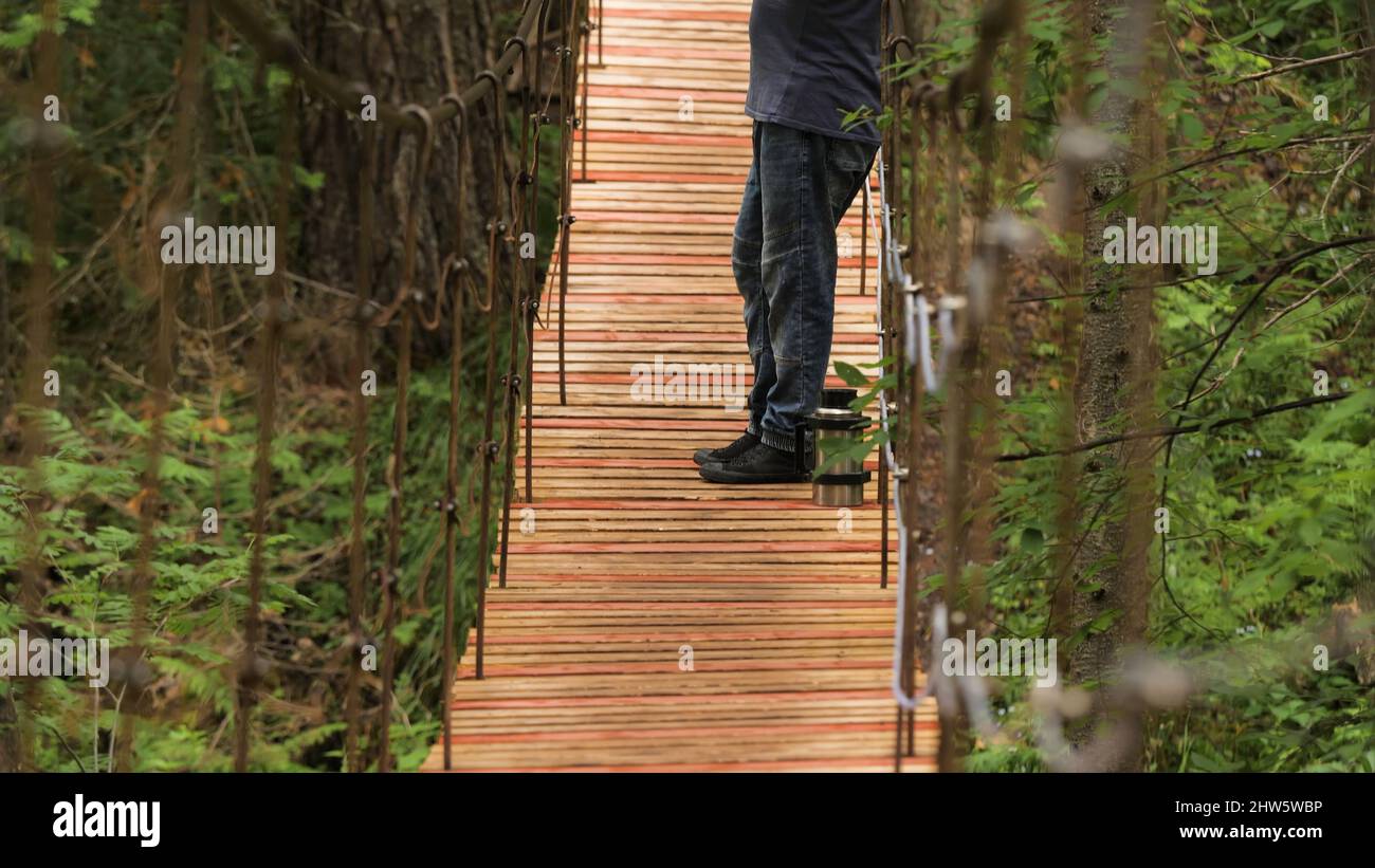 Le voyageur bénéficie d'une vue sur le pont suspendu. Films. L'homme s'est arrêté sur un pont en bois pour admirer la beauté de la nature. Homme fumant tuyau wh Banque D'Images