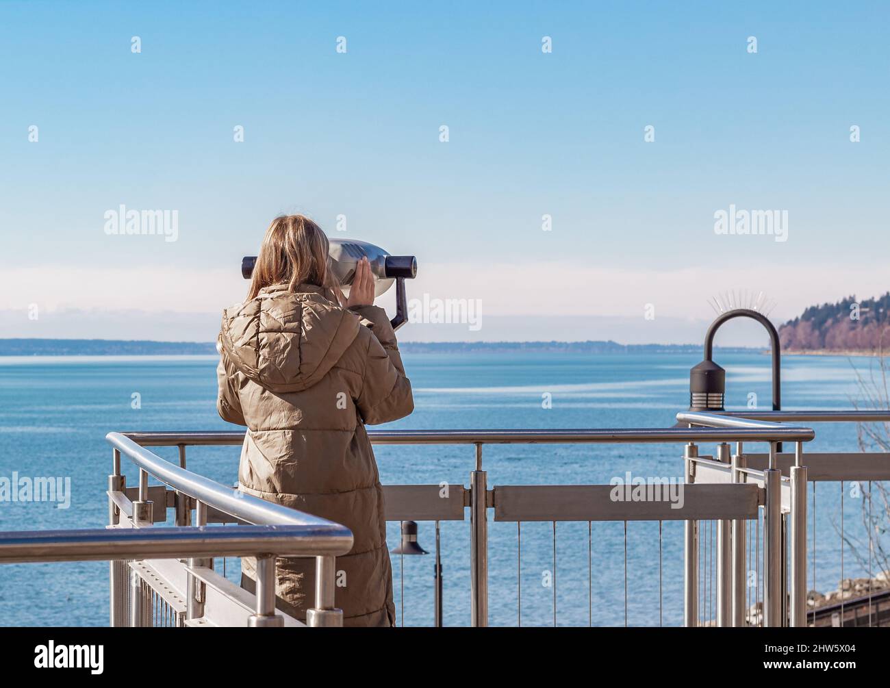 Jeune belle femme sur Un quai près de la mer regarde à travers les jumelles sur. Recherche de voyage concept de voyage Banque D'Images