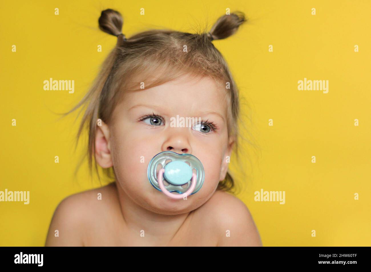 Portrait d'un enfant caucasien mignon petite fille de 2 ans avec sucette dans la bouche sur fond jaune Banque D'Images