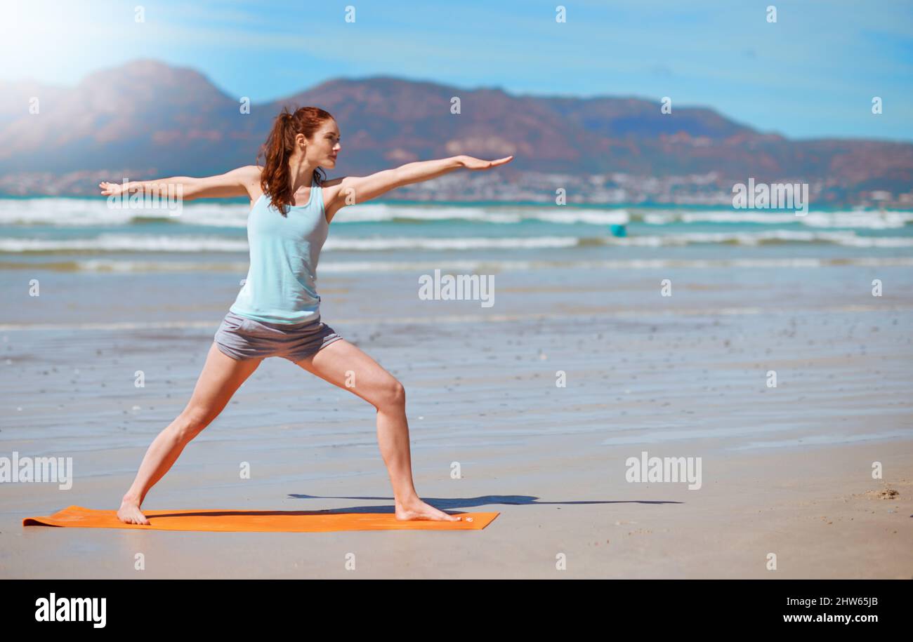 Soyez un guerrier pas un plus adoreur. Photo d'une jeune femme pratiquant sa routine de yoga à la plage. Banque D'Images
