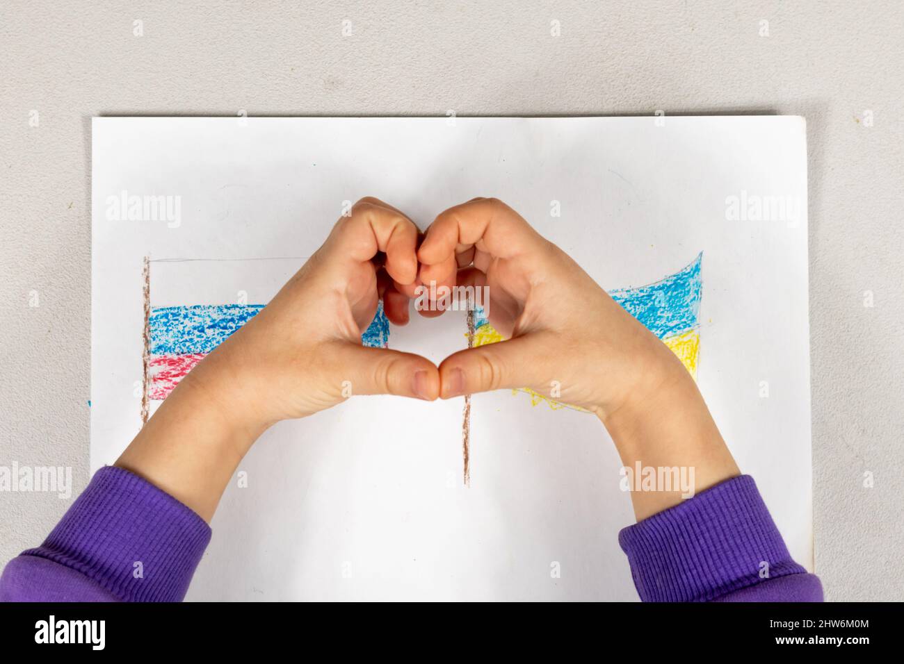 Un enfant fait un signe de coeur avec ses mains sur un dessin de deux drapeaux de l'Ukraine et de la Russie gros plan. Vue de dessus. Les enfants contre la guerre. Banque D'Images