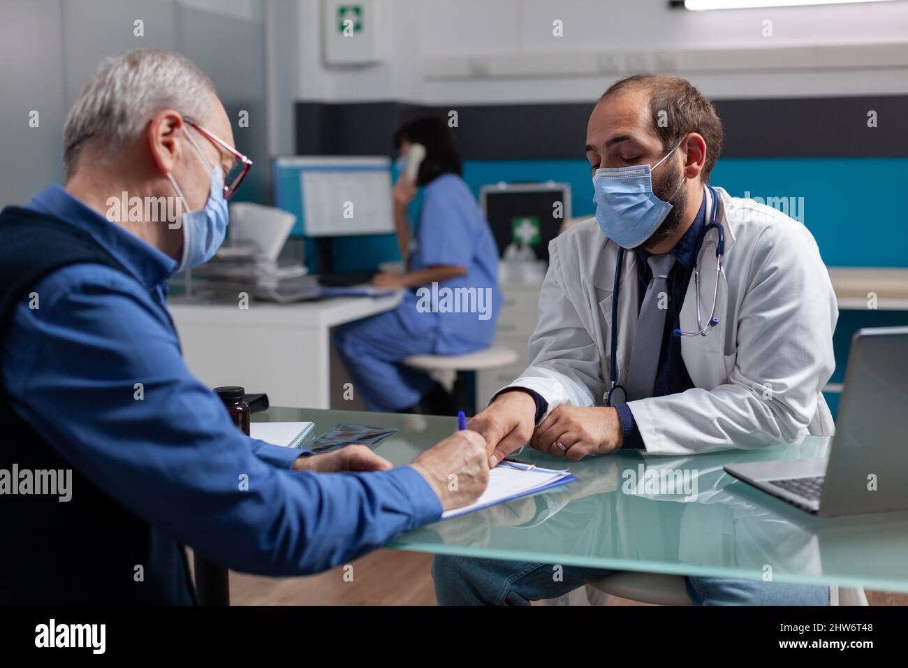 Un patient senior signe un rapport de consultation au bureau médical avec  un médecin, portant un masque facial. Homme aîné faisant la signature sur  le formulaire, rencontre avec le médecin généraliste à