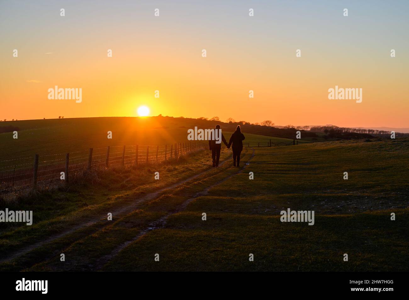 Heure d'or : un couple romantique se promenant main dans la main dans le soleil couchant le long du chemin sur South Downs Way près de Ditchling Beacon à Sussex, Angleterre. Banque D'Images