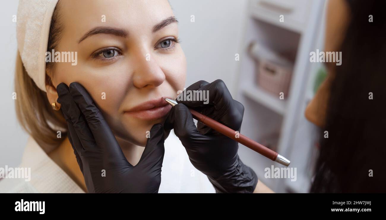 Jeune femme avec maquillage permanent sur ses lèvres dans un salon de cosmétologues. Tatouage de maquillage permanent. Dessinez une ligne avec un crayon rouge à lèvres Banque D'Images
