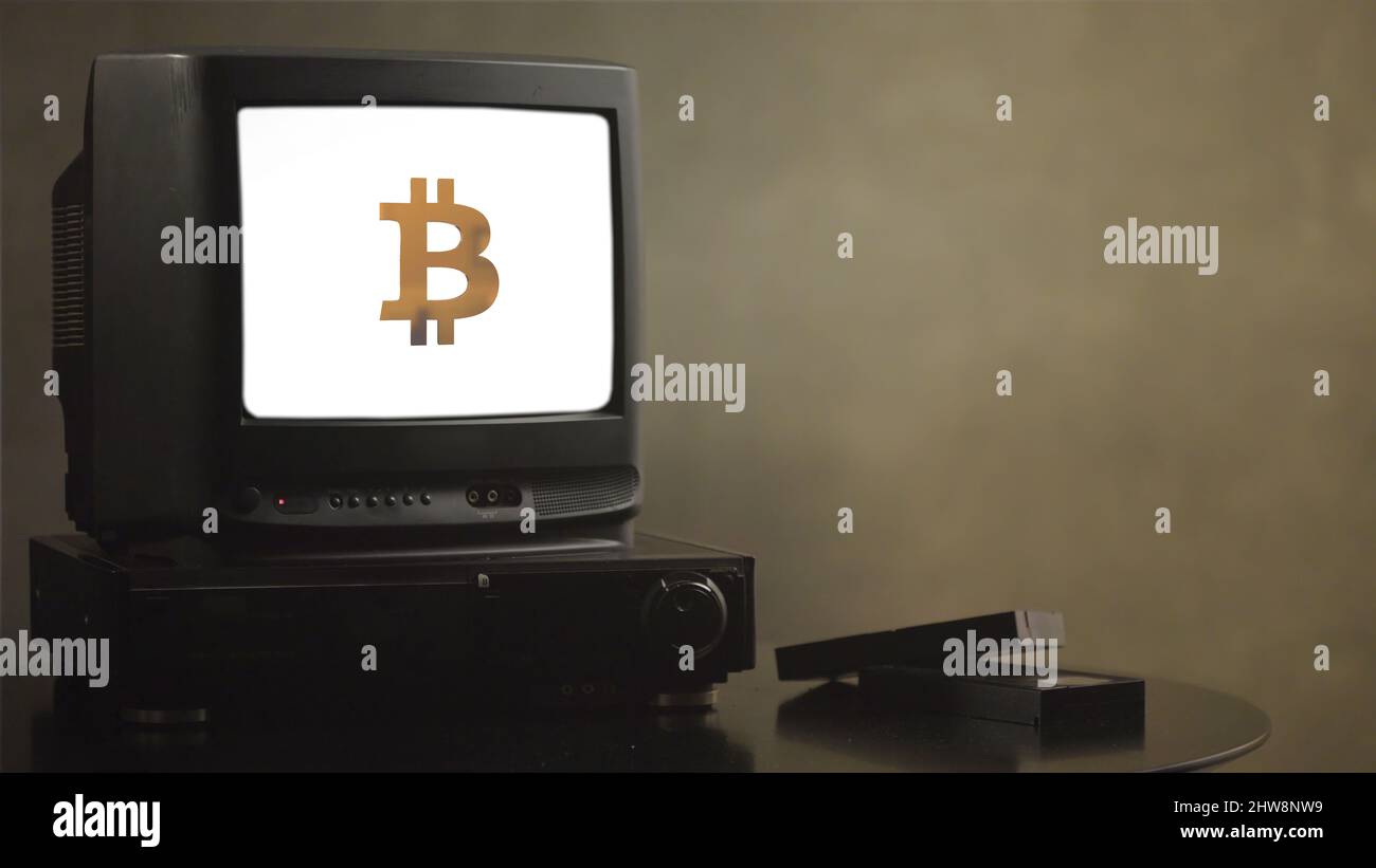 Téléviseur d'époque sur table en bois avec bitcoin. Vieux téléviseur avec bitcoin. Près du téléviseur, il y a des cassettes de film et un lecteur vidéo. Banque D'Images