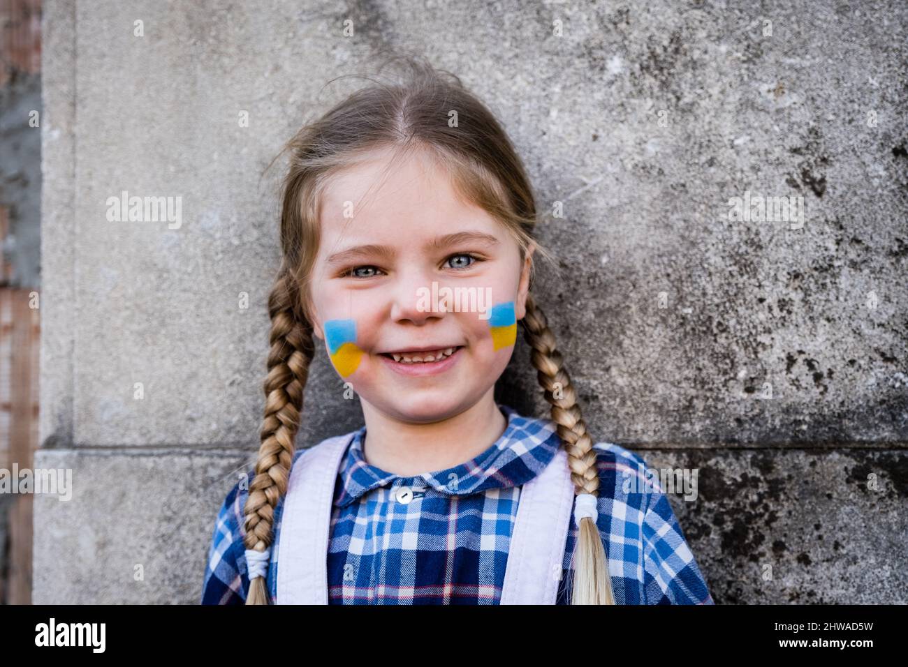 Portrait d'une fille effroyée avec drapeau peint sur la joue dans les couleurs jaune-bleu du drapeau ukrainien. Concept de paix et de protection des enfants Banque D'Images