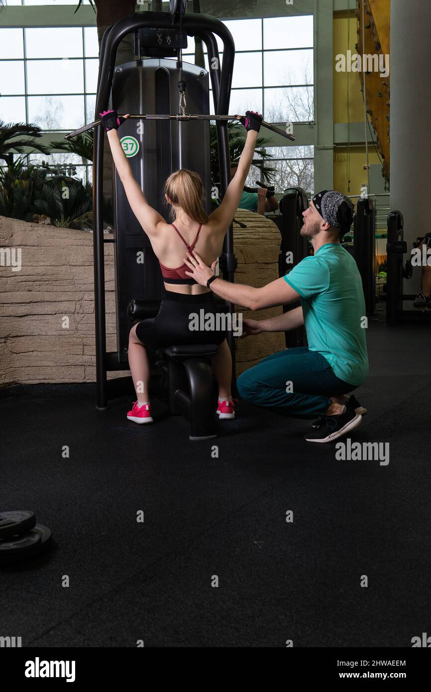 L'entraînement dirigé par un instructeur aide un beau client à effectuer des exercices dans un club de remise en forme, le concept de jouer du sport avec un loisir professionnel de gym Banque D'Images