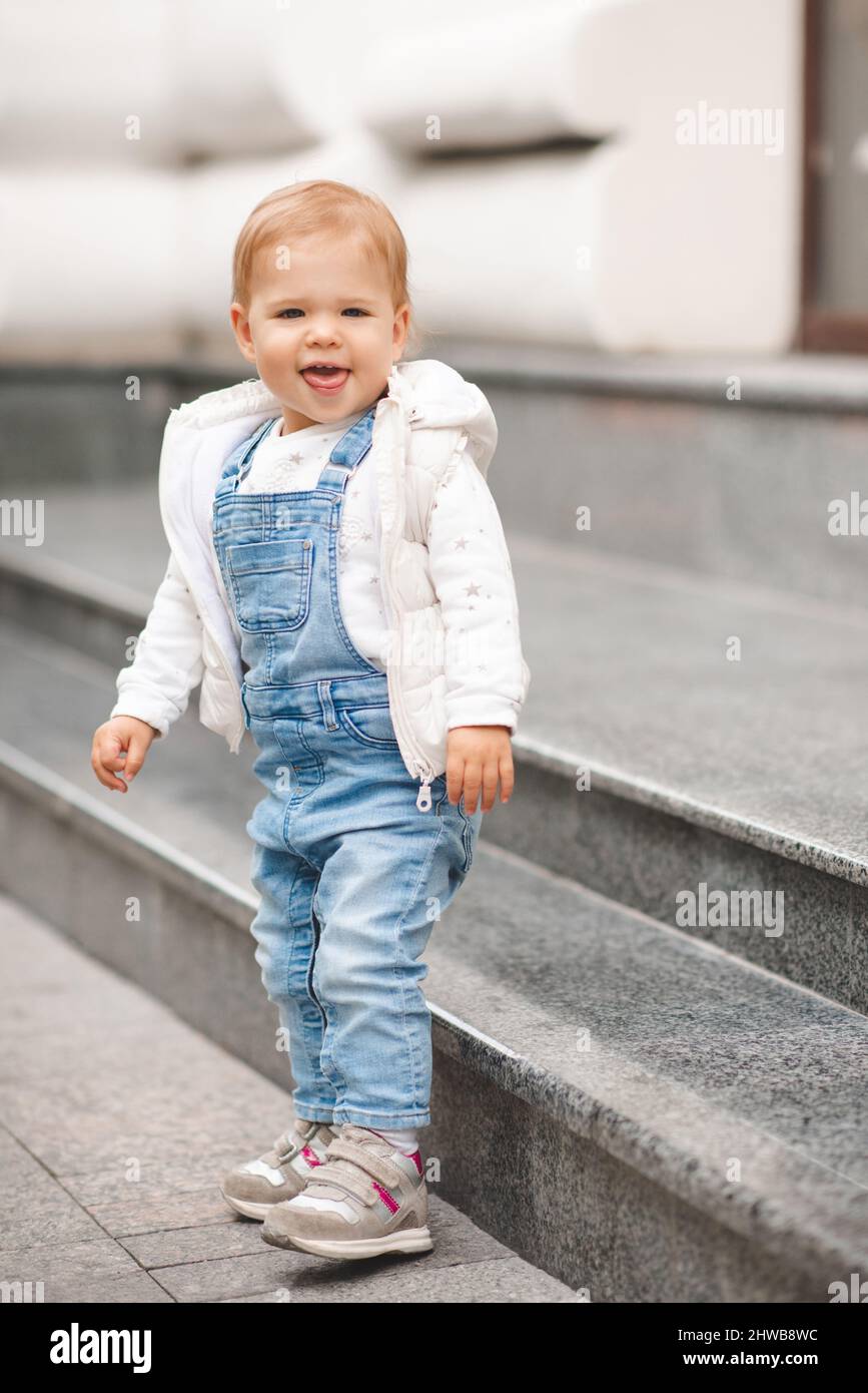 Mignon sourire bébé fille de 1-2 ans porter décontracté pantalon denim et  haut blanc dans la rue de ville dehors. Regarder l'appareil photo. Enfance.  Printemps Photo Stock - Alamy