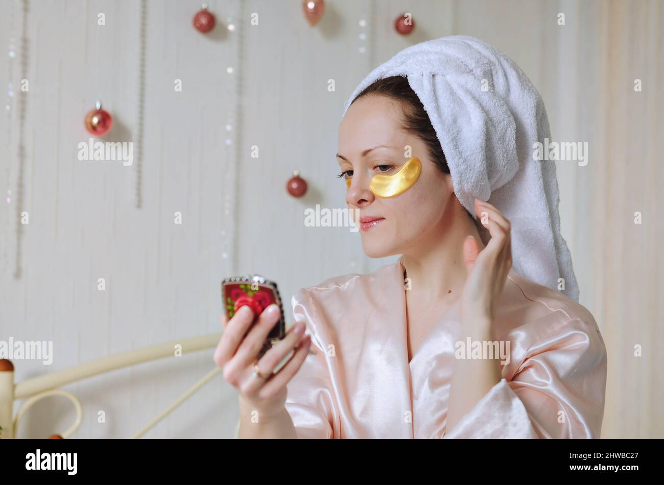 Jeune femme heureuse avec une serviette sur la tête faisant des procédures de soin de peau de visage. Lit en pyjama dans une maison confortable avec téléphone. Technologie. Médias sociaux Banque D'Images
