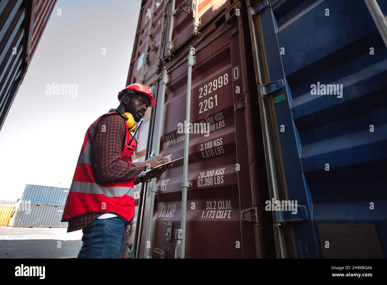 Travailleur afro-américain tenant des tablettes et contrôlant le chargement des conteneurs de fret à partir d'un navire de fret de fret pour l'exportation d'importation. Banque D'Images