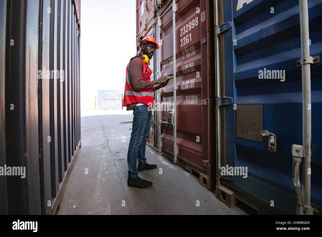 Travailleur afro-américain tenant des tablettes et contrôlant le chargement des conteneurs de fret à partir d'un navire de fret de fret pour l'exportation d'importation. Banque D'Images