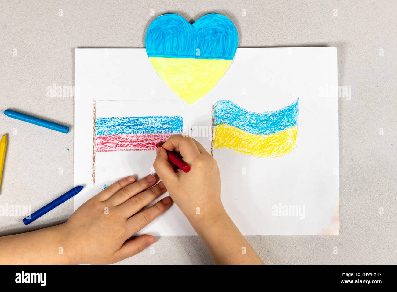Un enfant fait un signe de coeur avec ses mains sur un dessin de deux drapeaux de l'Ukraine et de la Russie gros plan. Vue de dessus. Les enfants contre la guerre. Banque D'Images