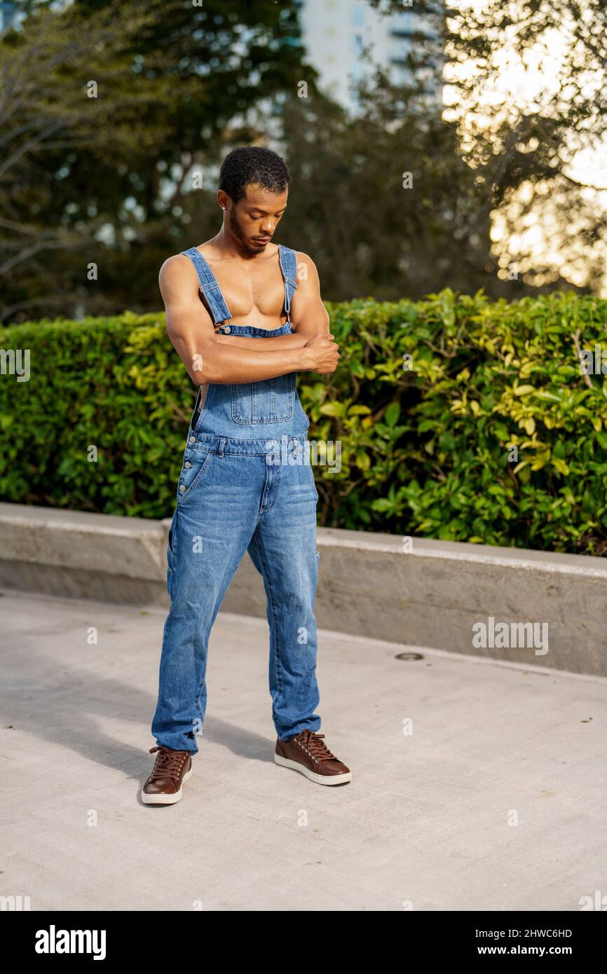 Beau jeune homme noir posant dans des salopettes dans le parc Banque D'Images