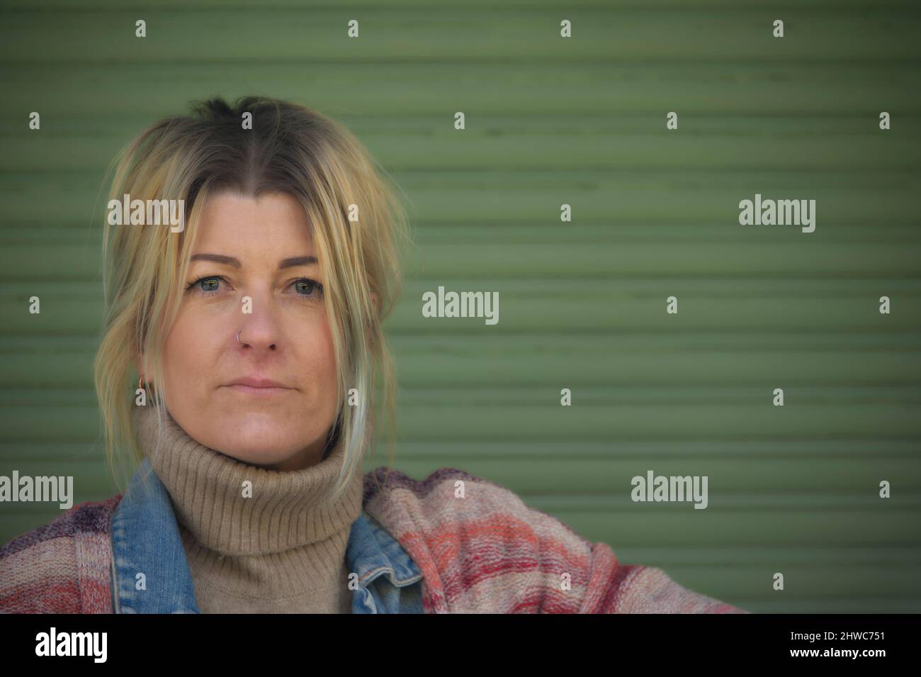 Portrait d'une femme blonde avec des yeux bleus verts regardant l'appareil photo sur un fond vert Banque D'Images