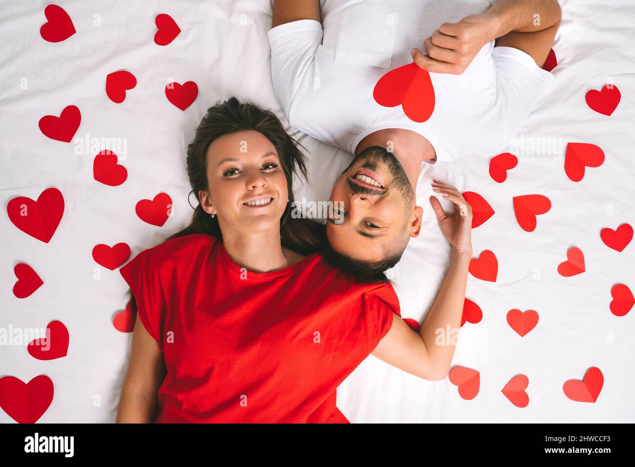 Vue de dessus d'un beau couple amoureux allongé sur le lit avec des coeurs en papier rouge Banque D'Images