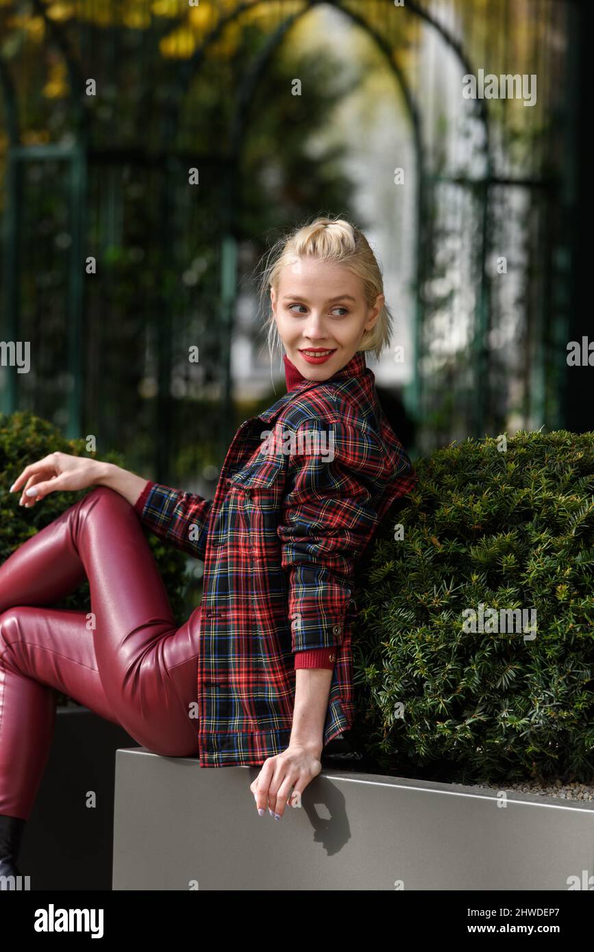 fille blonde à la mode avec un rouge à lèvres posant à l'extérieur . Vêtu  d'un leggings en cuir rouge, d'une veste à col roulé et à carreaux. Figure  parfaite Photo Stock -