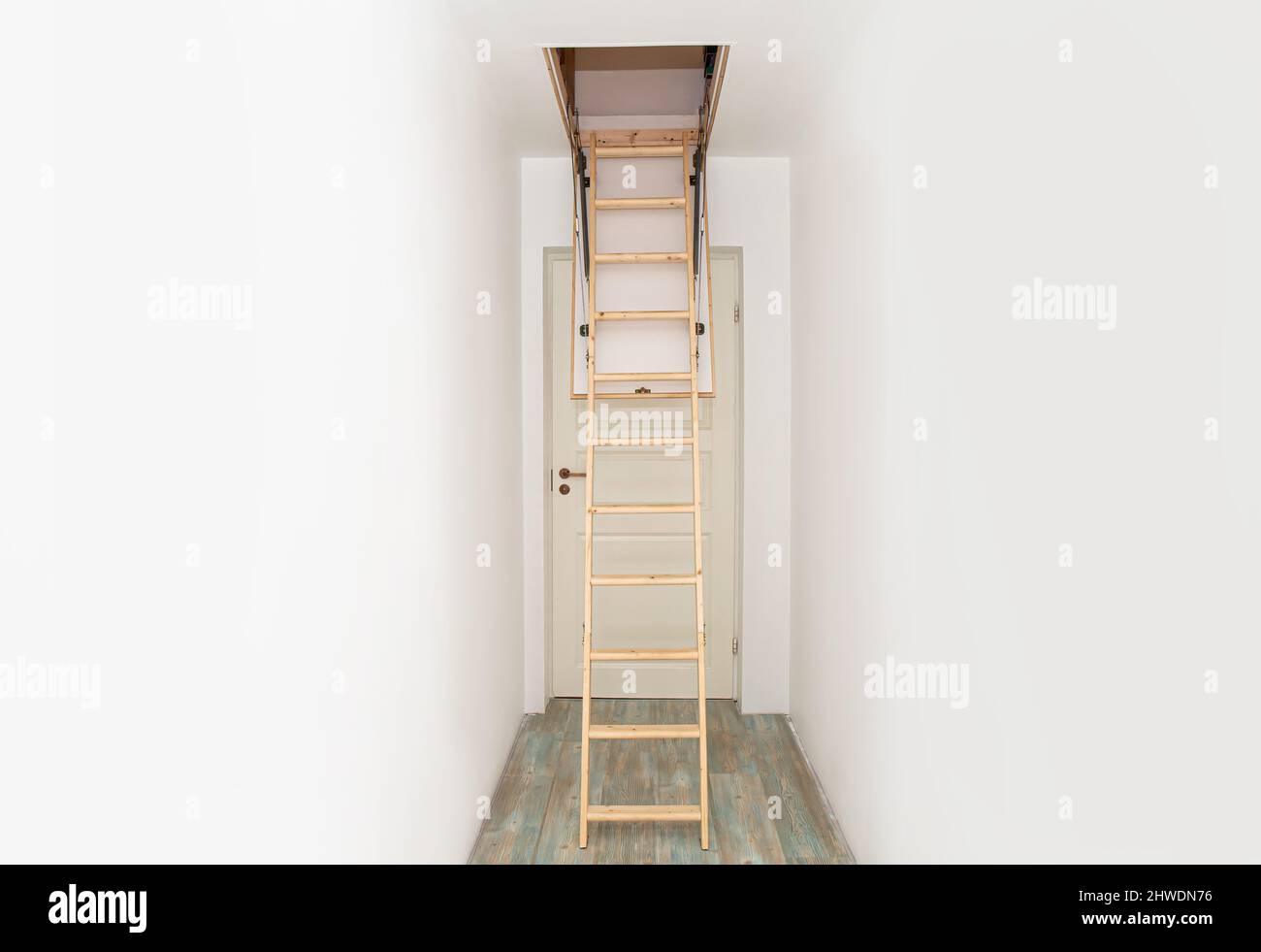 Escalier en bois pliable à monter dans le grenier échelle dans le couloir blanc vide de la maison. Couloir étroit avec murs blancs et sol stratifié bleu. Banque D'Images